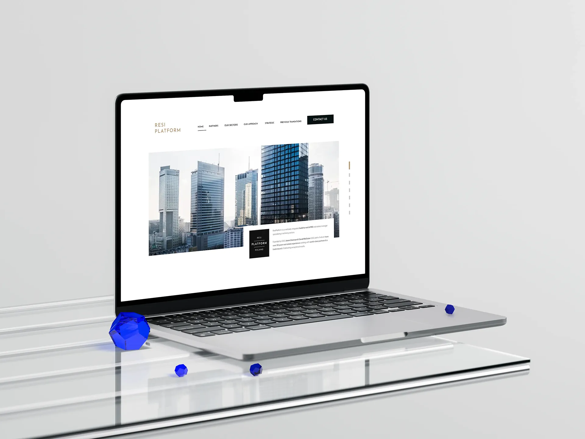 Makieta strony ResiPlatform wyświetlona na laptopie MacBook stojącym na szklanej powierzchni, obok niebieskie kryształy na jasnym tle.