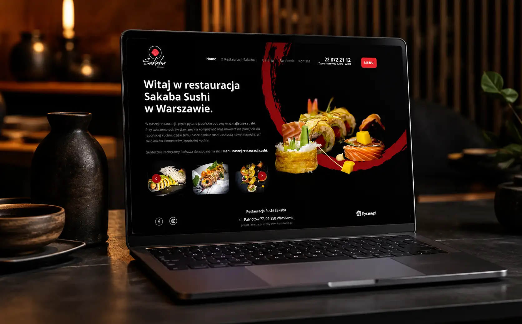 Makieta strony internetowej restauracji sushi Sakaba wyświetlona na laptopie MacBook stojącym na drewnianym stole; ciemny motyw z czerwonymi akcentami i zdjęciami dań sushi.